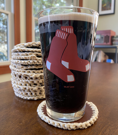 A Red Sox pint glass rests on a coaster with a crocheted edge, in honor of Garrett Crochet.
